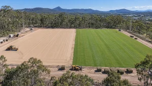 Aerial view of a Queensland sports field being built, half levelled sand rootzone and half new turf, with machinery and pallets